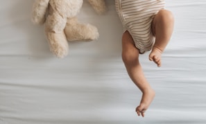 a baby laying on a bed next to a teddy bear