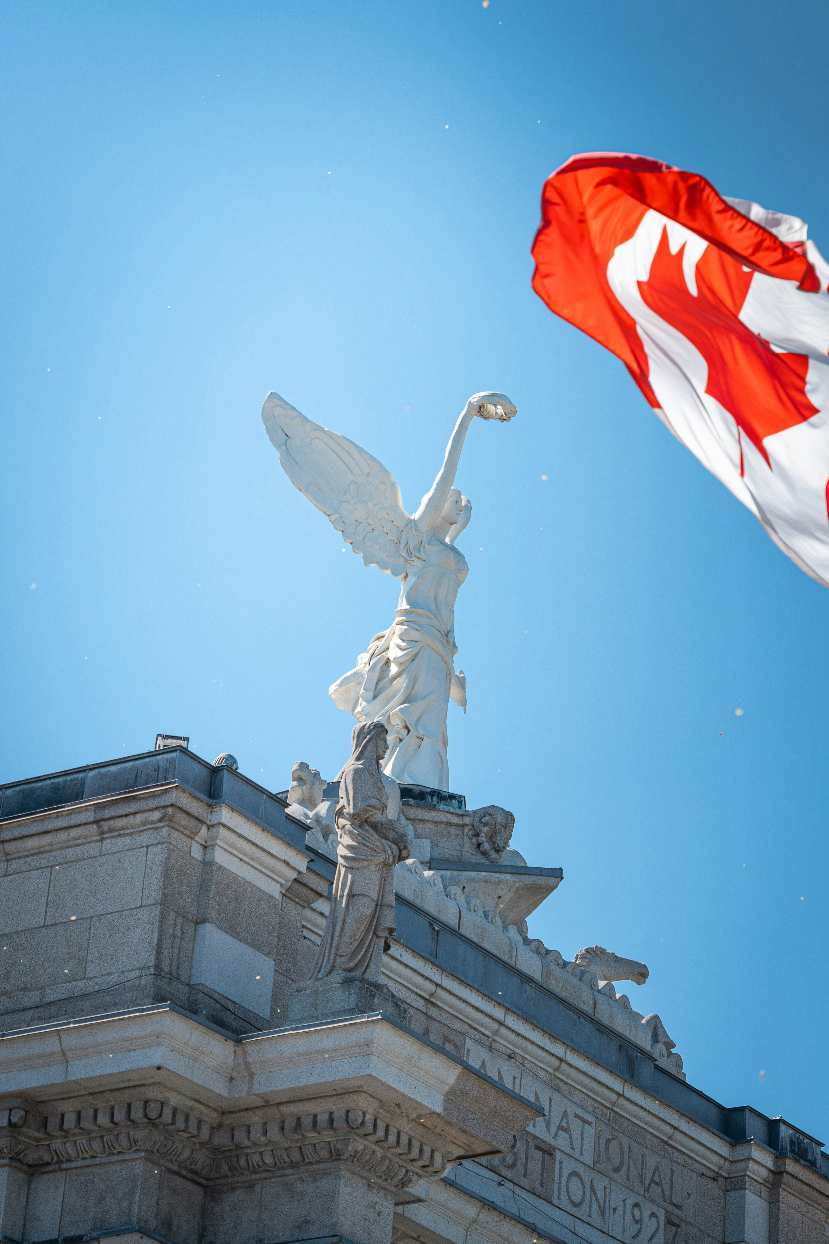 a canadian flag flying next to a statue on top of a building