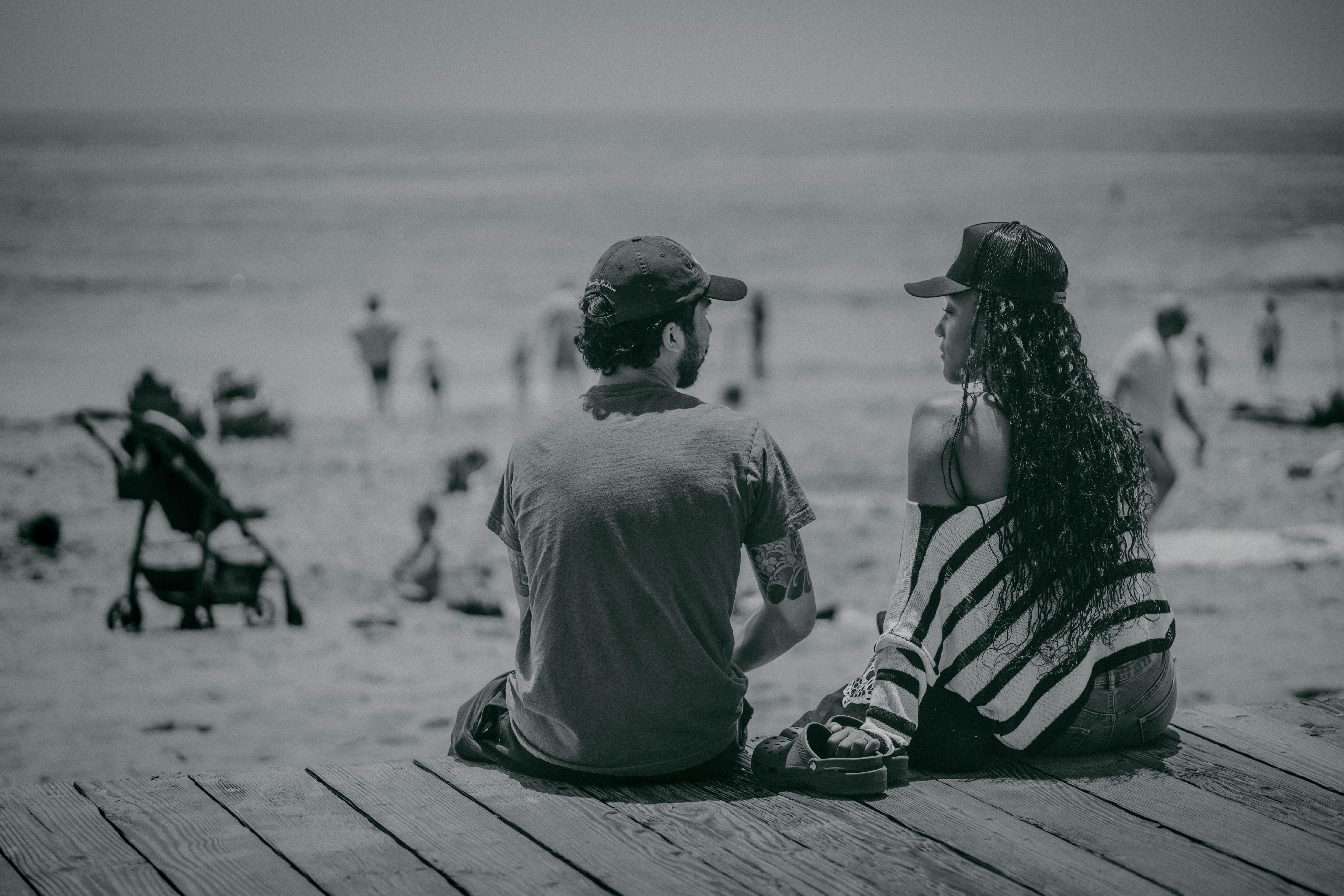 a man and a woman sitting on a pier looking at the beach