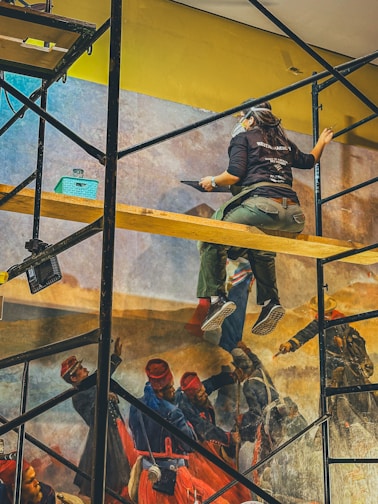 a man sitting on a scaffold in front of a painting