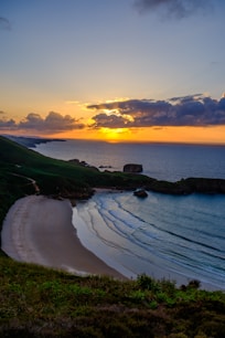 the sun is setting over the ocean and a sandy beach
