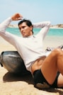 a man sitting on the beach with his hands behind his head