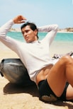 a man sitting on the beach with his hands behind his head