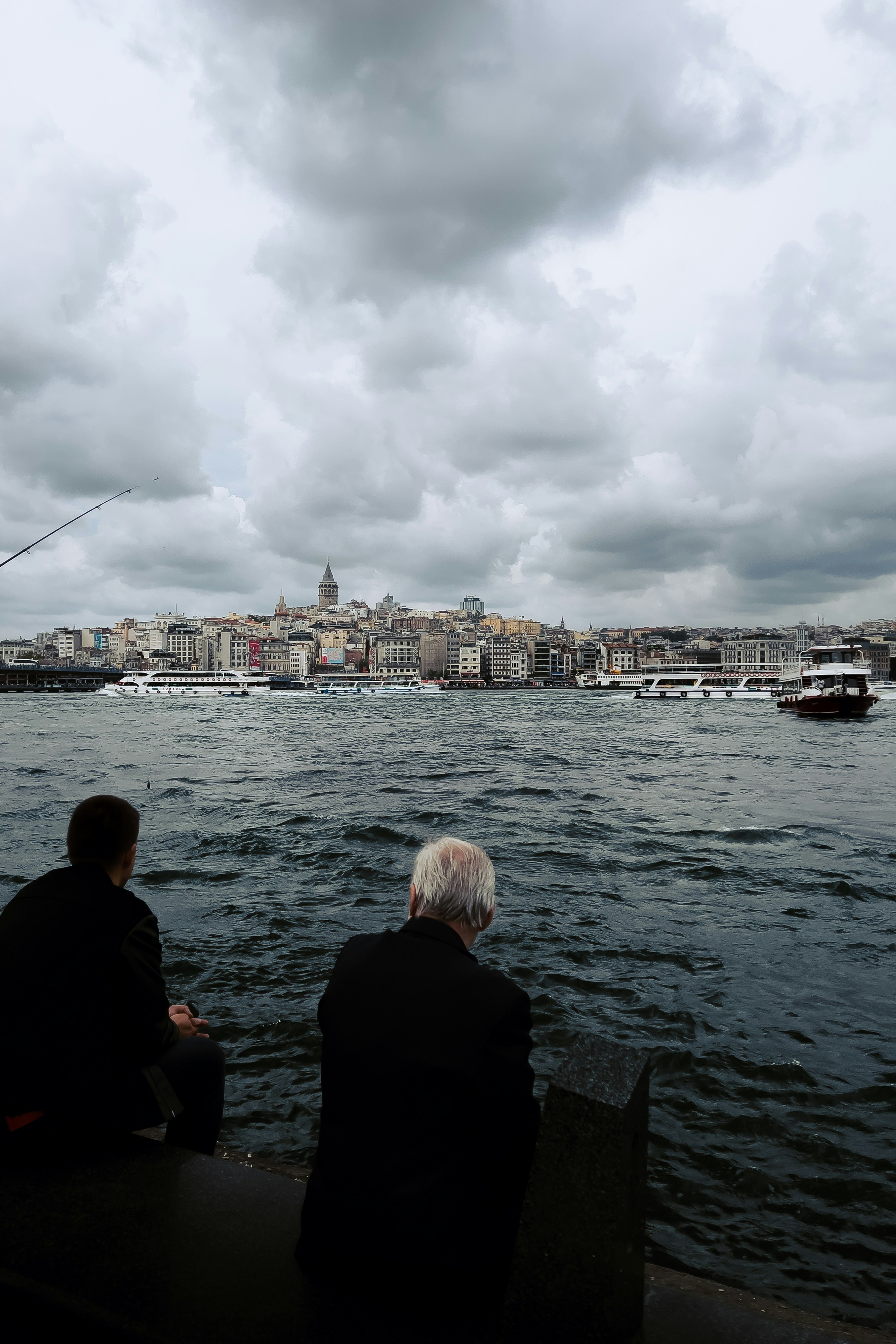 A couple of people sitting on a bench next to a body of water photo ...