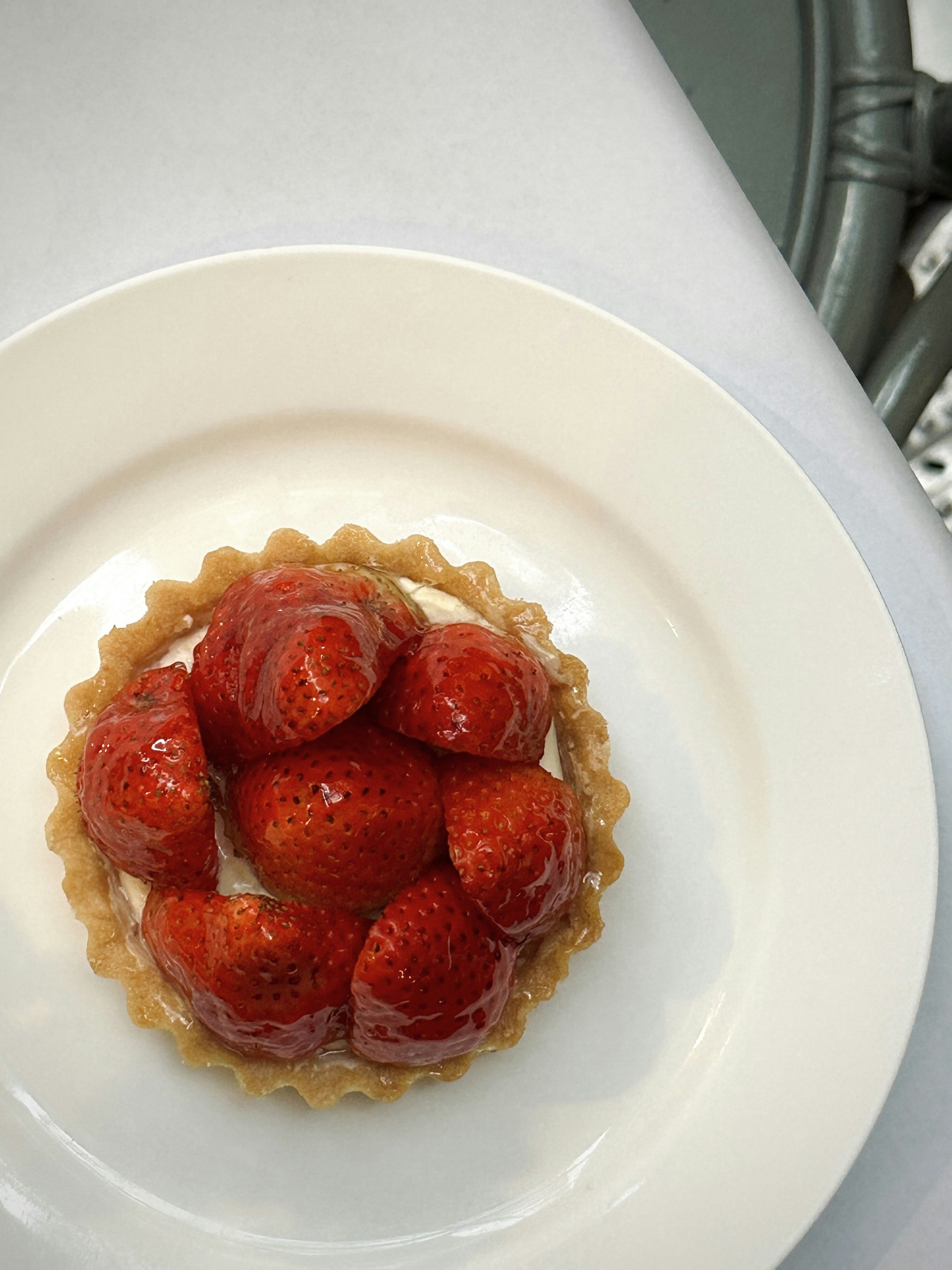 Glazed strawberry tart with cream filling on white ceramic plate, natural window light