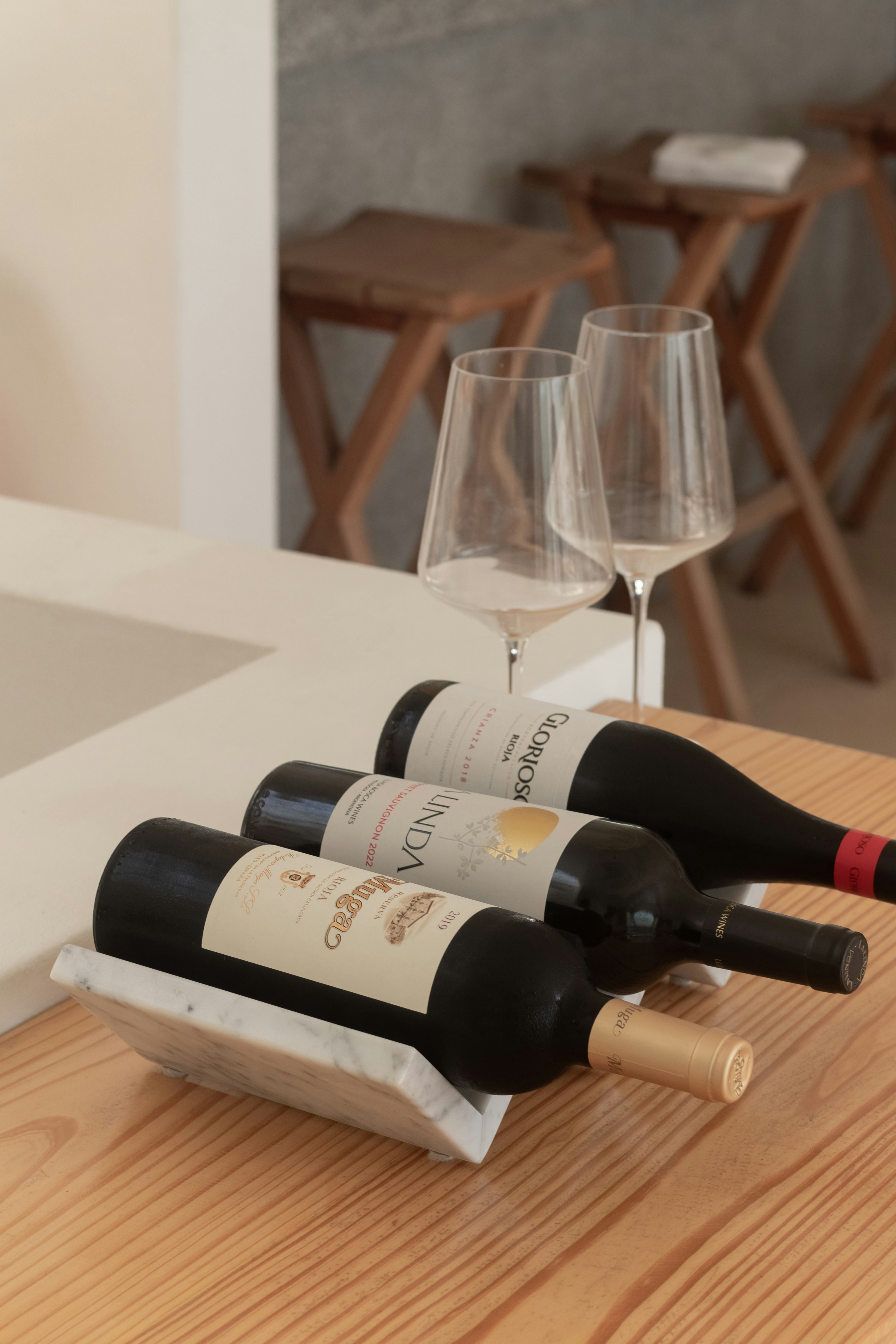 Three dark wine bottles on a marble holder with wine glasses.