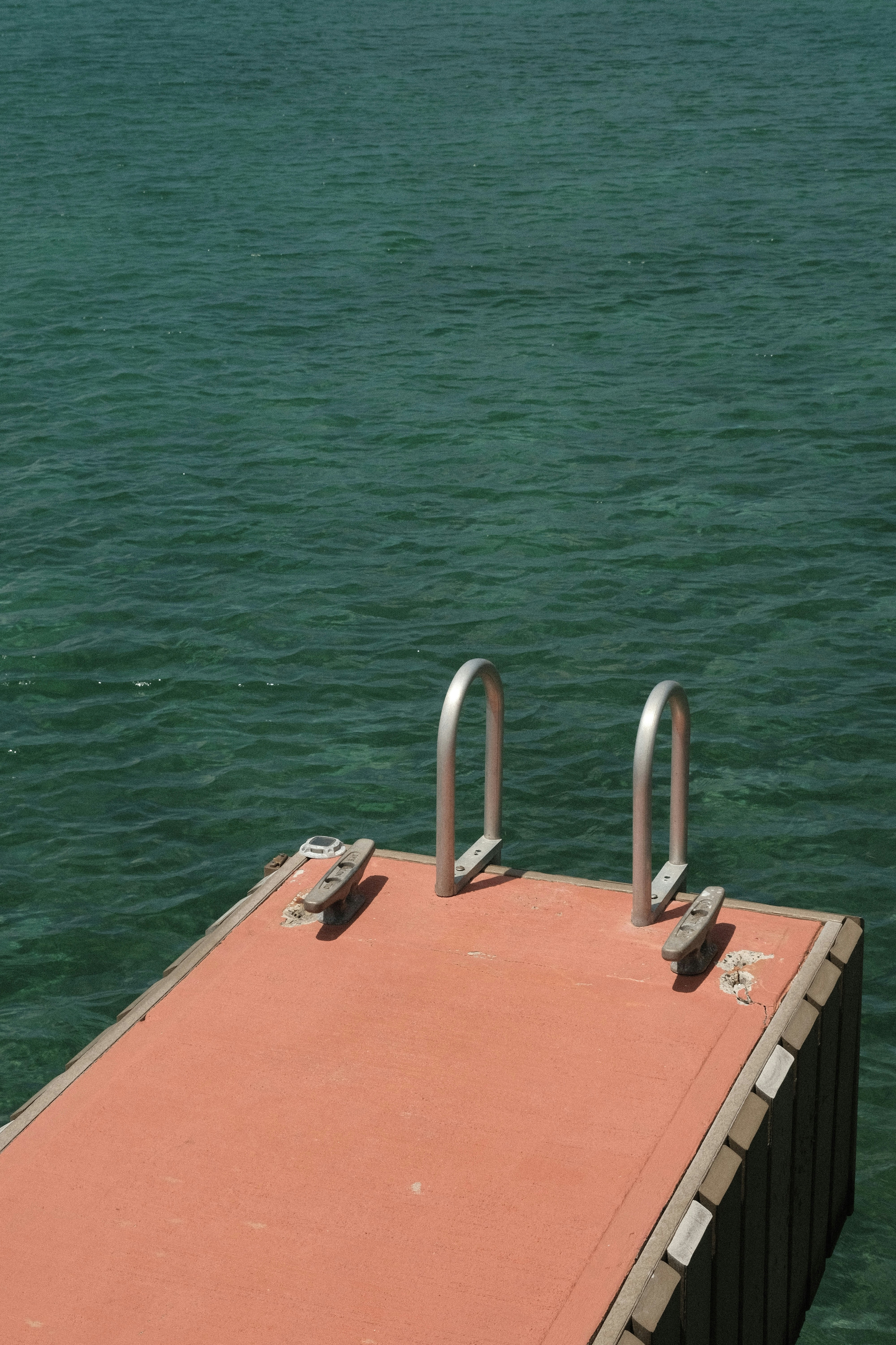 a red dock with two metal railings in the middle of a body of water