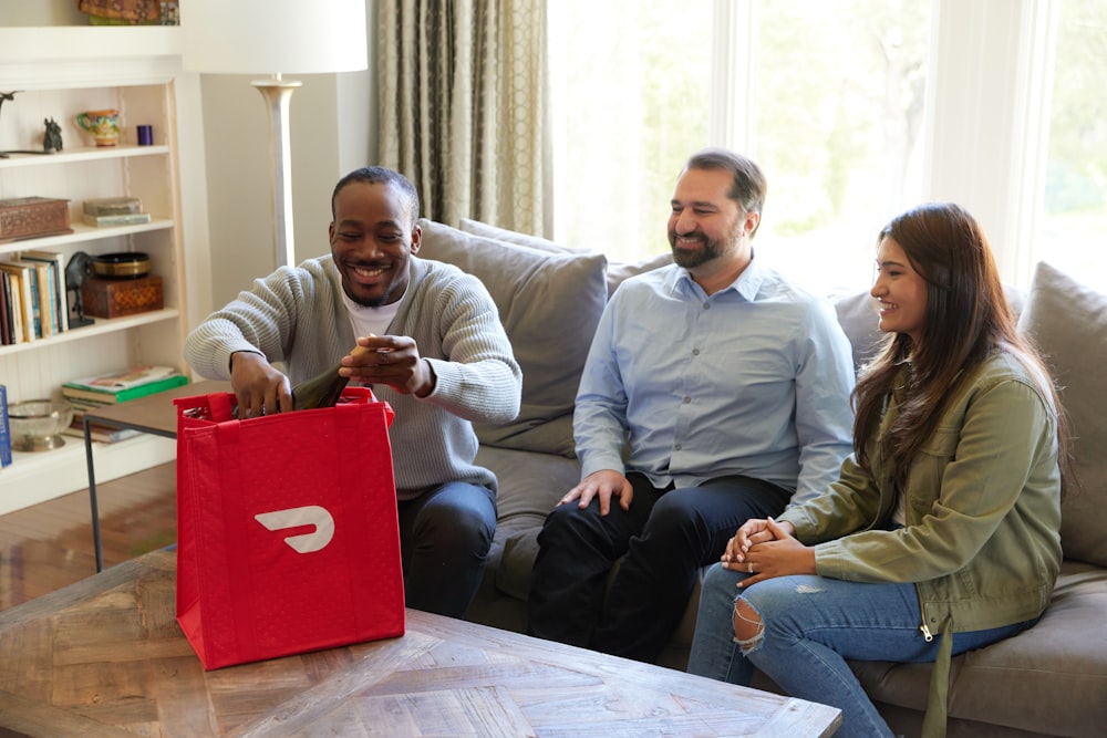 three people sitting on a couch with a red bag