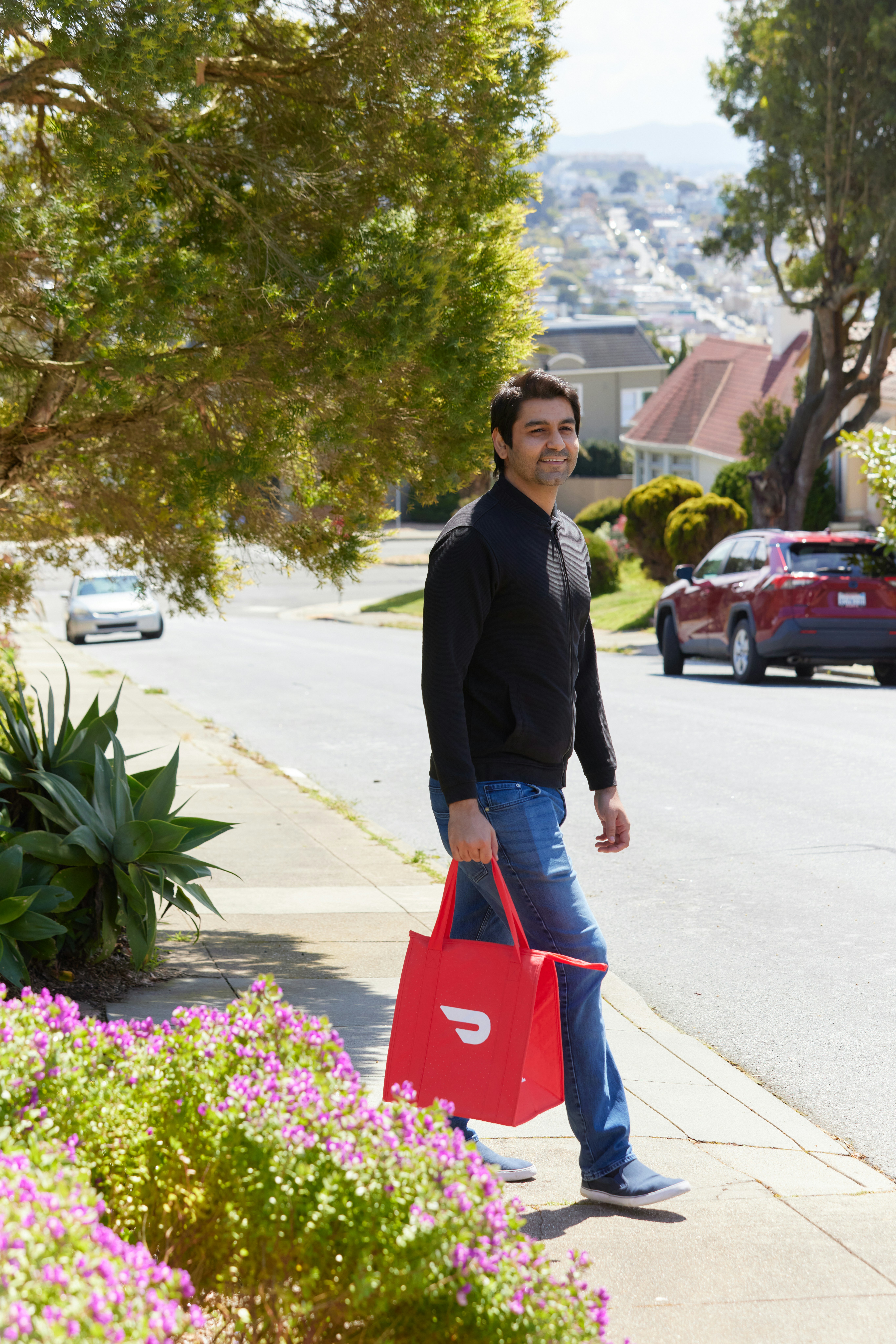 a man walking down a sidewalk carrying a red bag