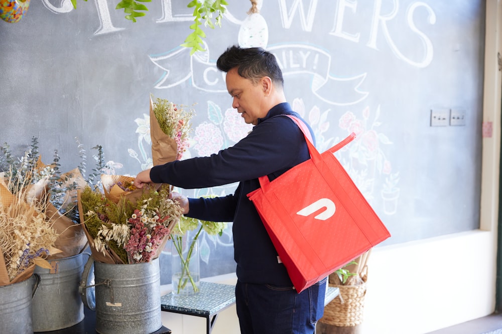 Un hombre sosteniendo una bolsa roja de compras cerca de un ramo de flores