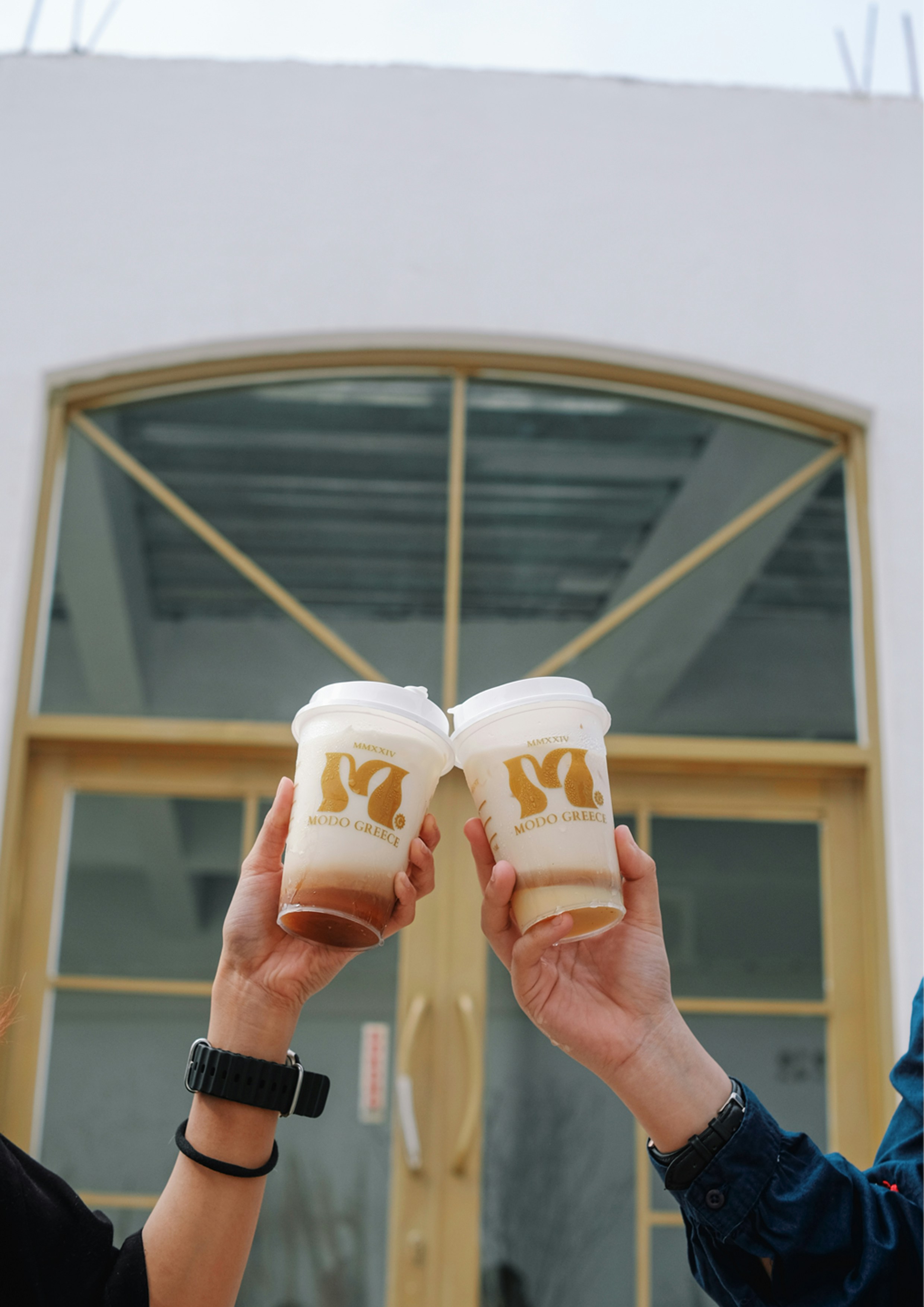 建物の前でコーヒーカップを掲げる2人