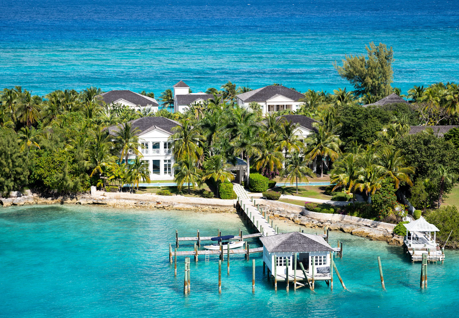 Aerial view of a private Bahamian cay, a house set among palms above a long dock reaching into turquoise shallows