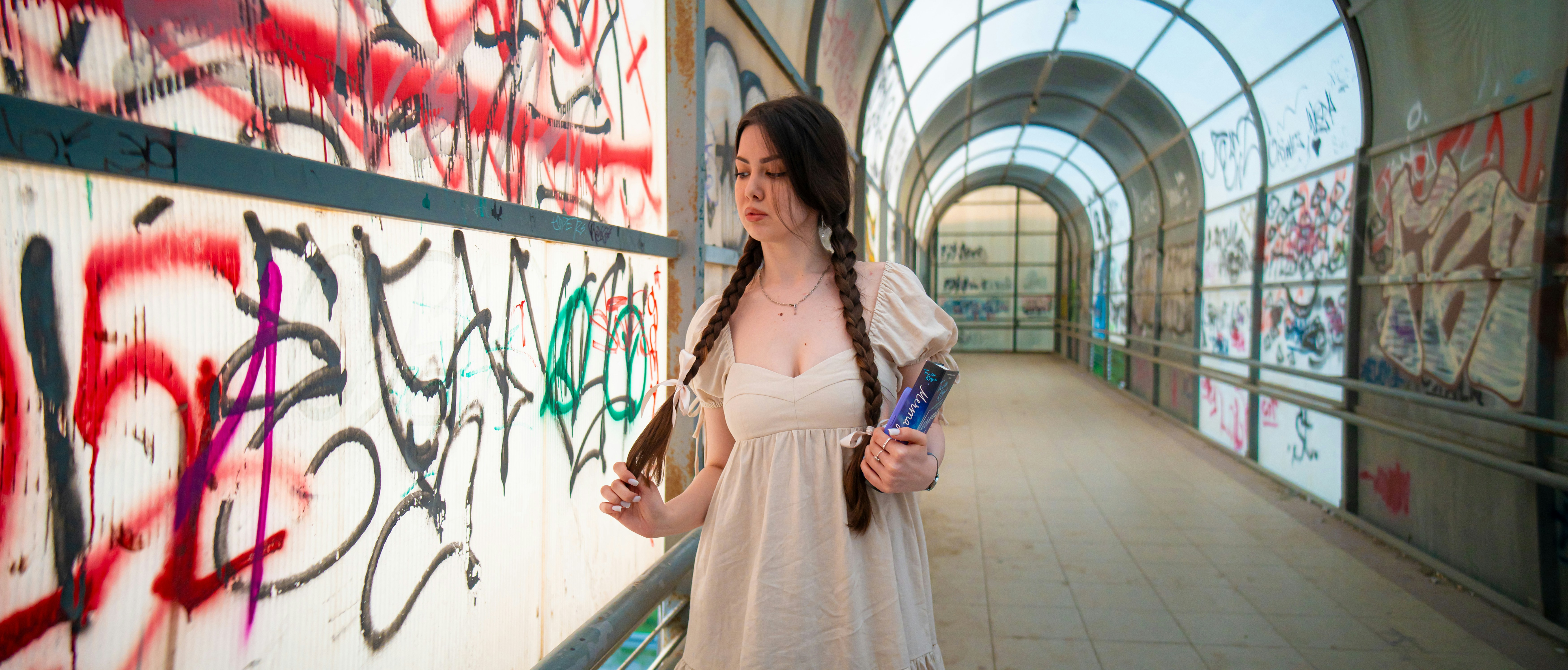 una mujer con un vestido blanco de pie junto a una pared cubierta de grafitis