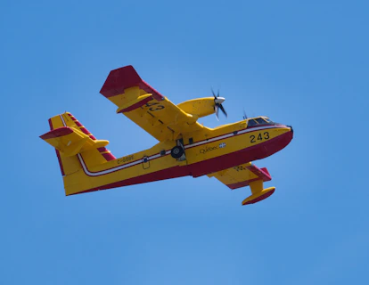 a yellow and red plane flying through a blue sky