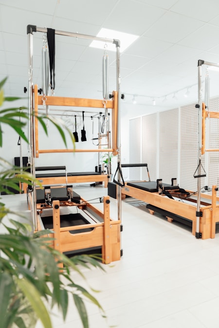 Row of wooden Pilates reformers with springs, straps, and towers in a bright studio