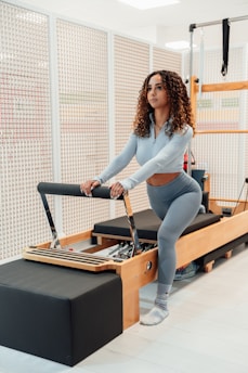 uma mulher com blusa cinza e legging em um aparelho de pilates