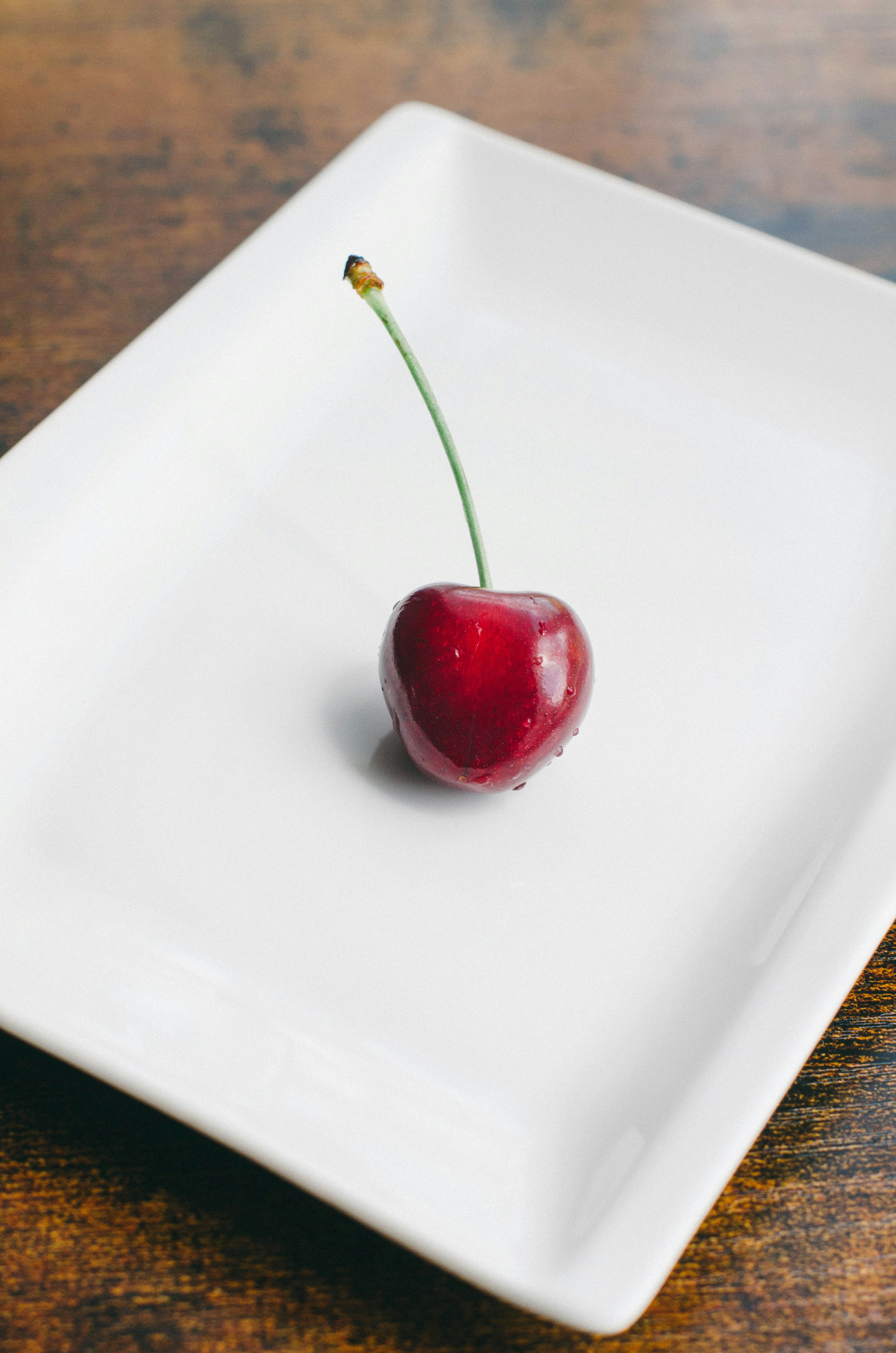 白いお皿の上に乗せた一輪のさくらんぼ