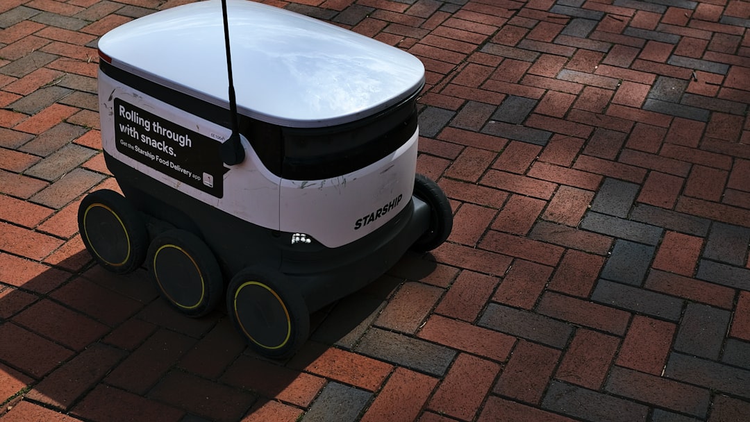 a white and black robot sitting on top of a brick road, A Starship autonomous food delivery robot traveling on campus gr