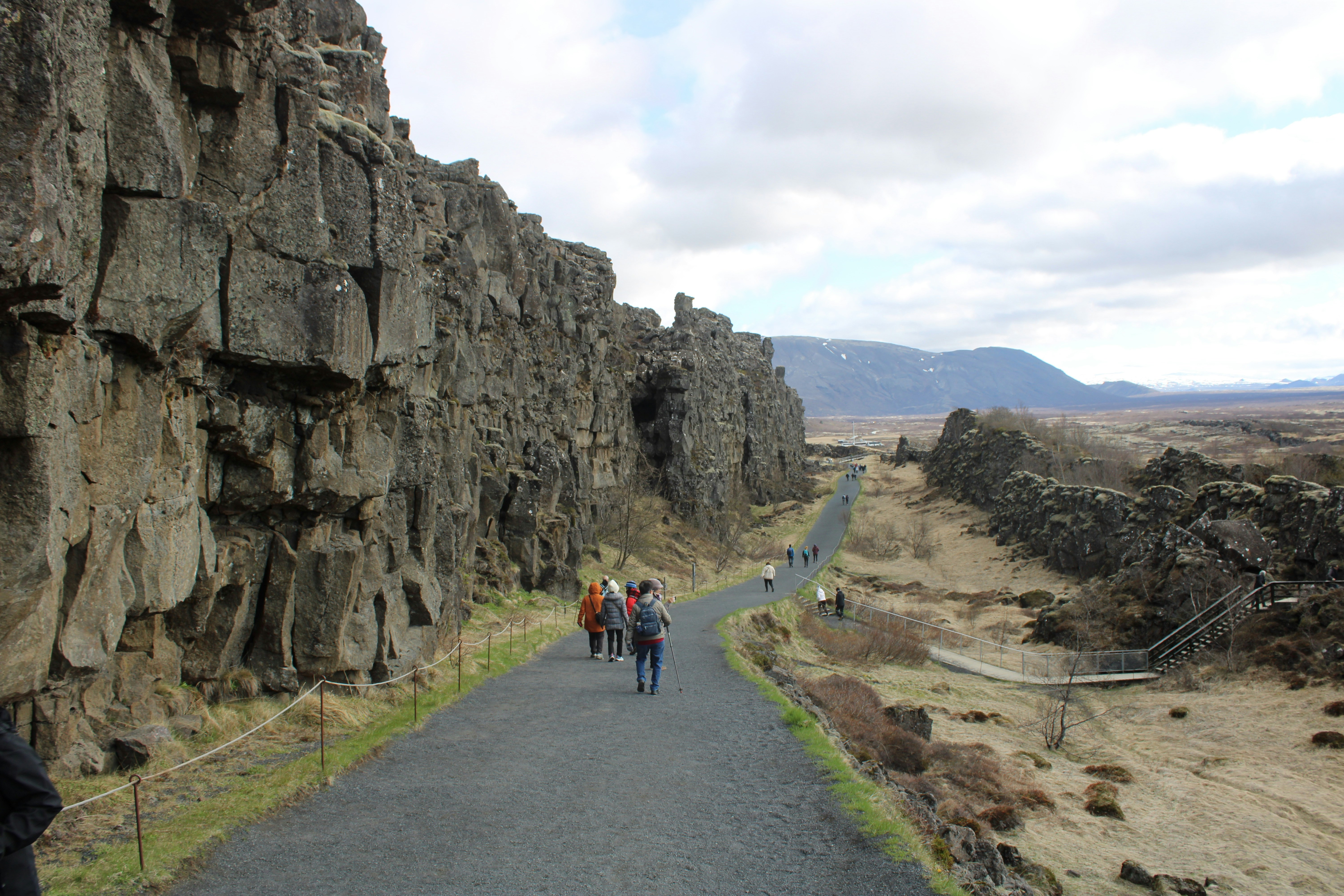 a group of people walking down a road next to a cliff
