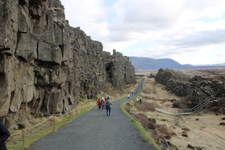 a group of people walking down a road next to a cliff