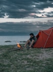 a man sitting in front of a tent next to a fire