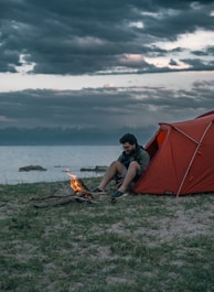 a man sitting in front of a tent next to a fire