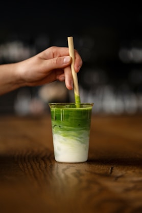 a hand holding a wooden stick over a green drink