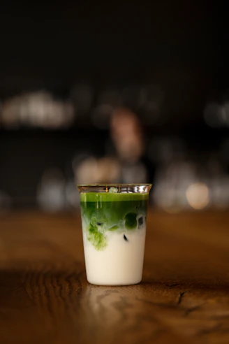 a shot glass filled with green liquid on top of a wooden table