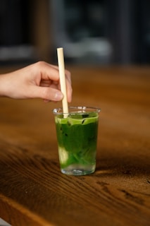 a hand holding a toothpick over a green drink
