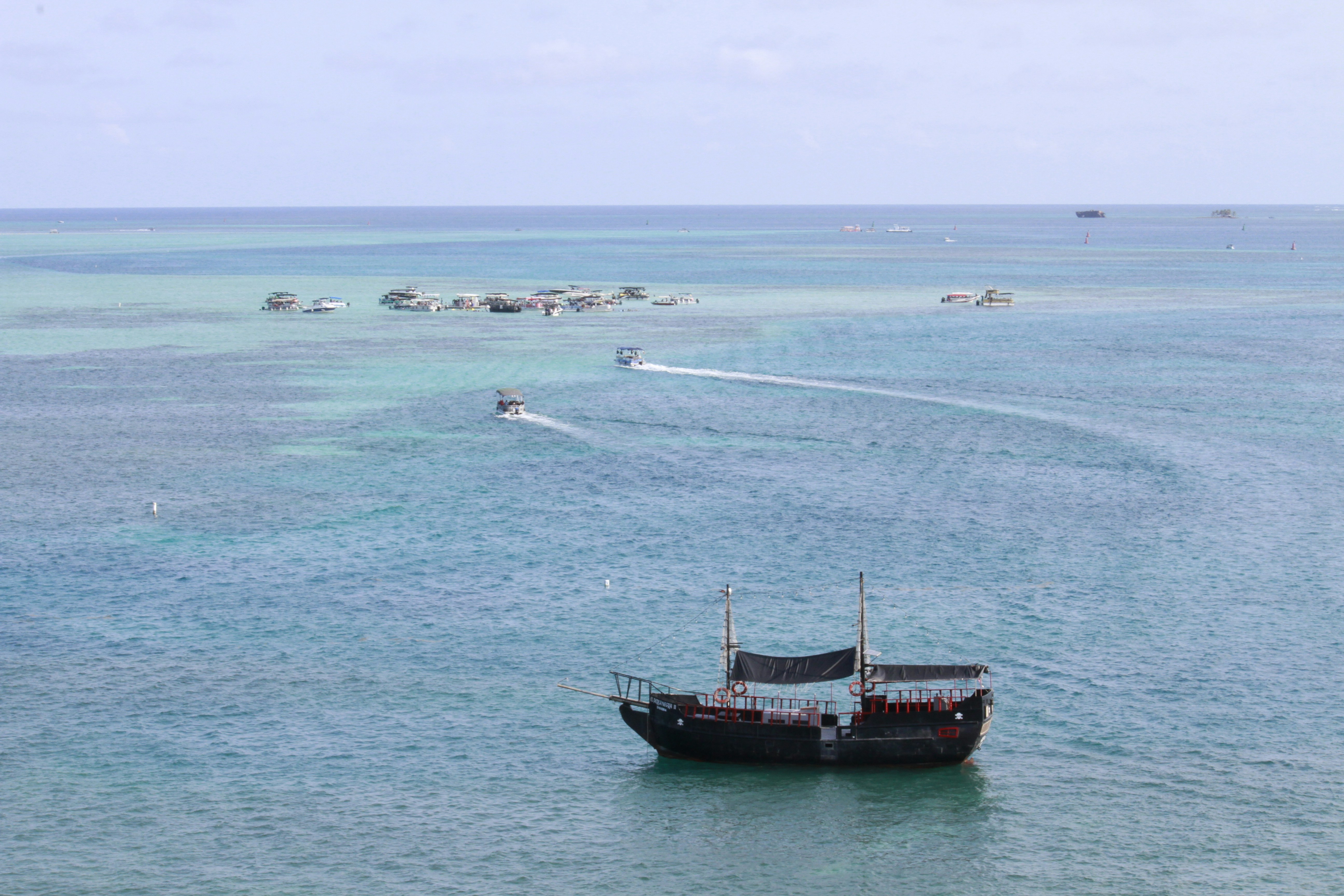 a boat in the middle of a body of water, Vista De Barco e Islote en el mar de 7 colores de san andres islas en Colombia.