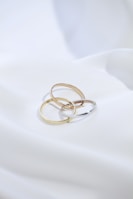 two gold rings sitting on top of a white sheet