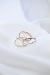 two gold rings sitting on top of a white sheet