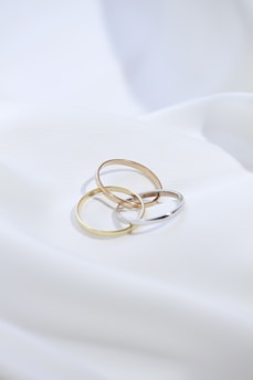 two gold rings sitting on top of a white sheet