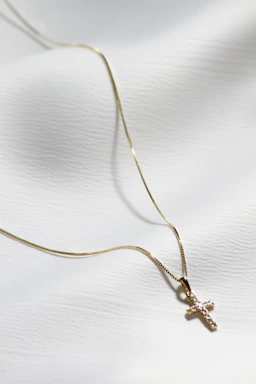 a gold cross necklace on a white cloth