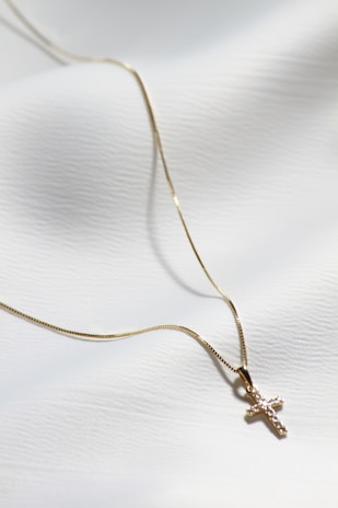 a gold cross necklace on a white cloth
