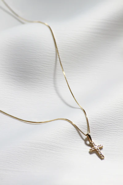 a gold cross necklace on a white cloth