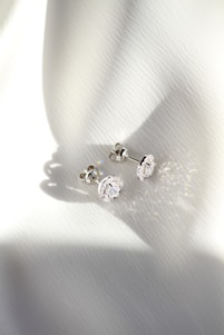 a pair of diamond earrings sitting on top of a white cloth