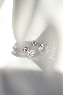 a pair of diamond earrings sitting on top of a white cloth