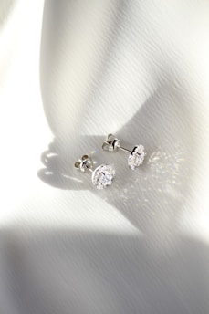 a pair of diamond earrings sitting on top of a white cloth