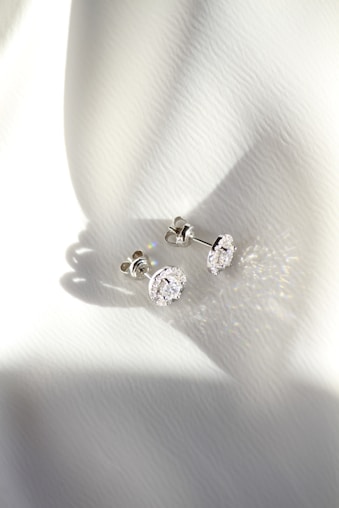 a pair of diamond earrings sitting on top of a white cloth