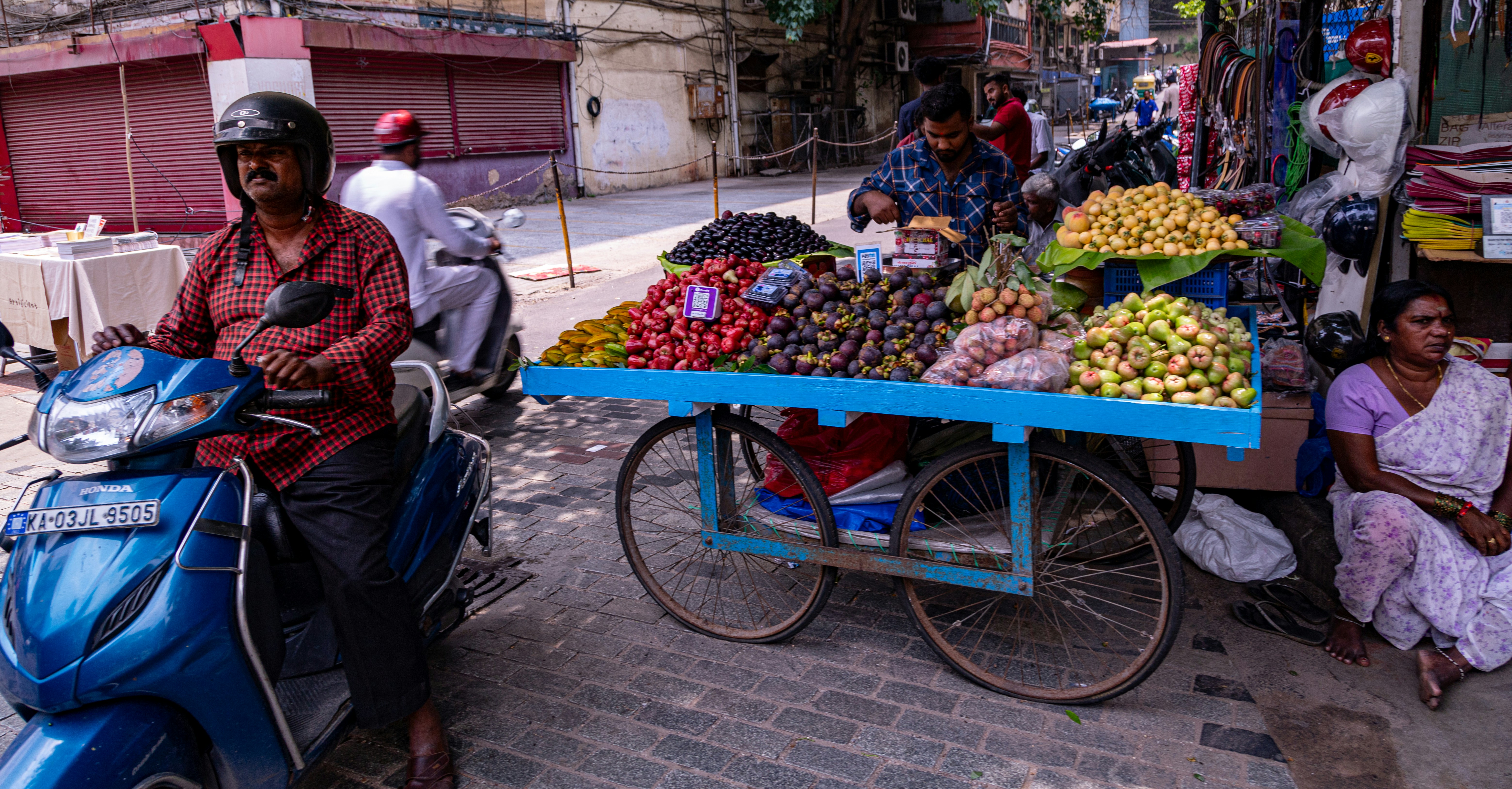 a man riding a scooter past a fruit stand