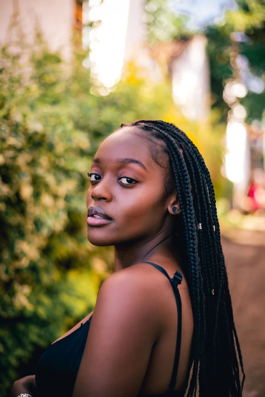 A woman outdoors looking over her shoulder with long braids down her back.