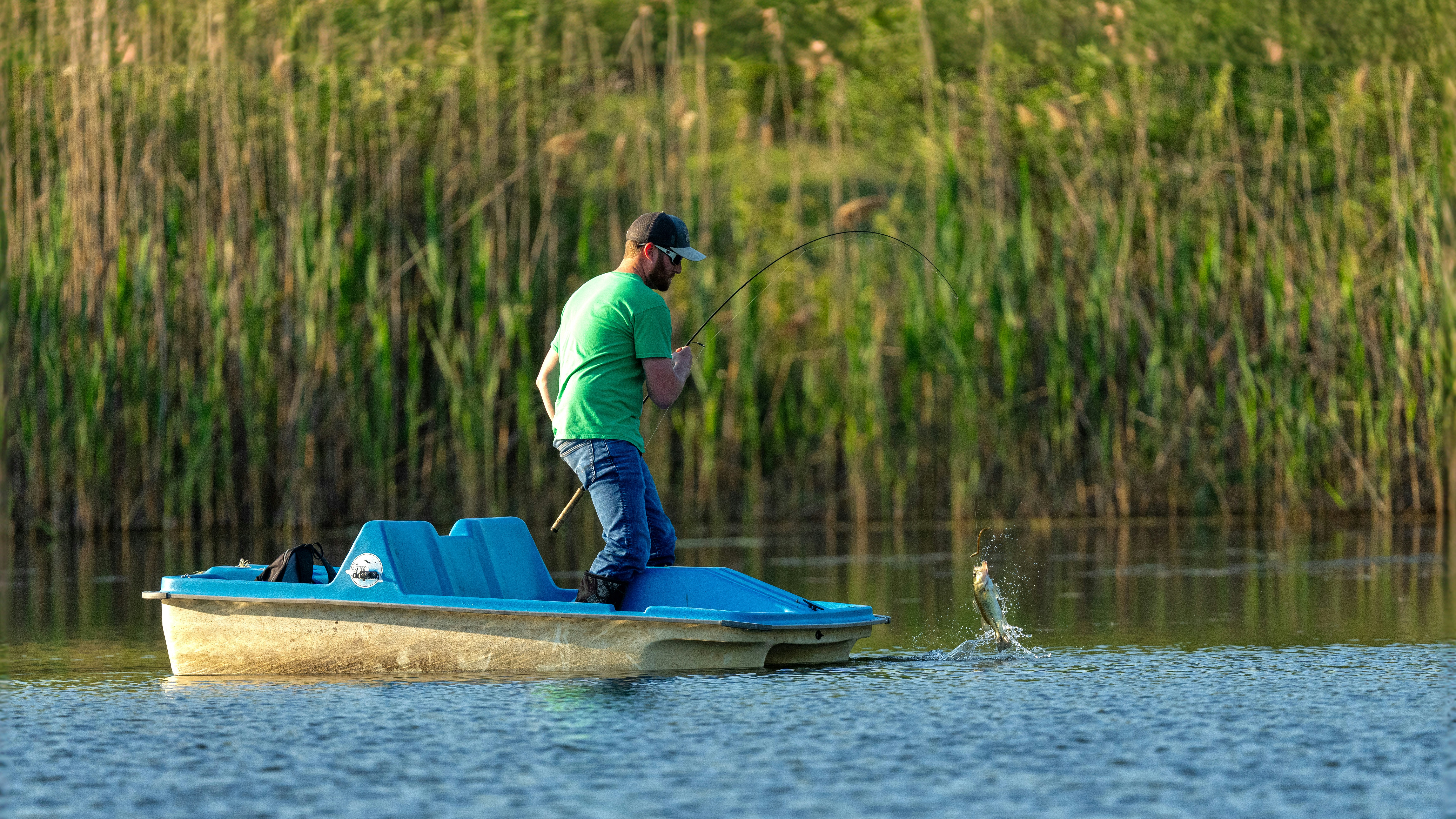 un uomo in camicia verde che pesca su una barca blu