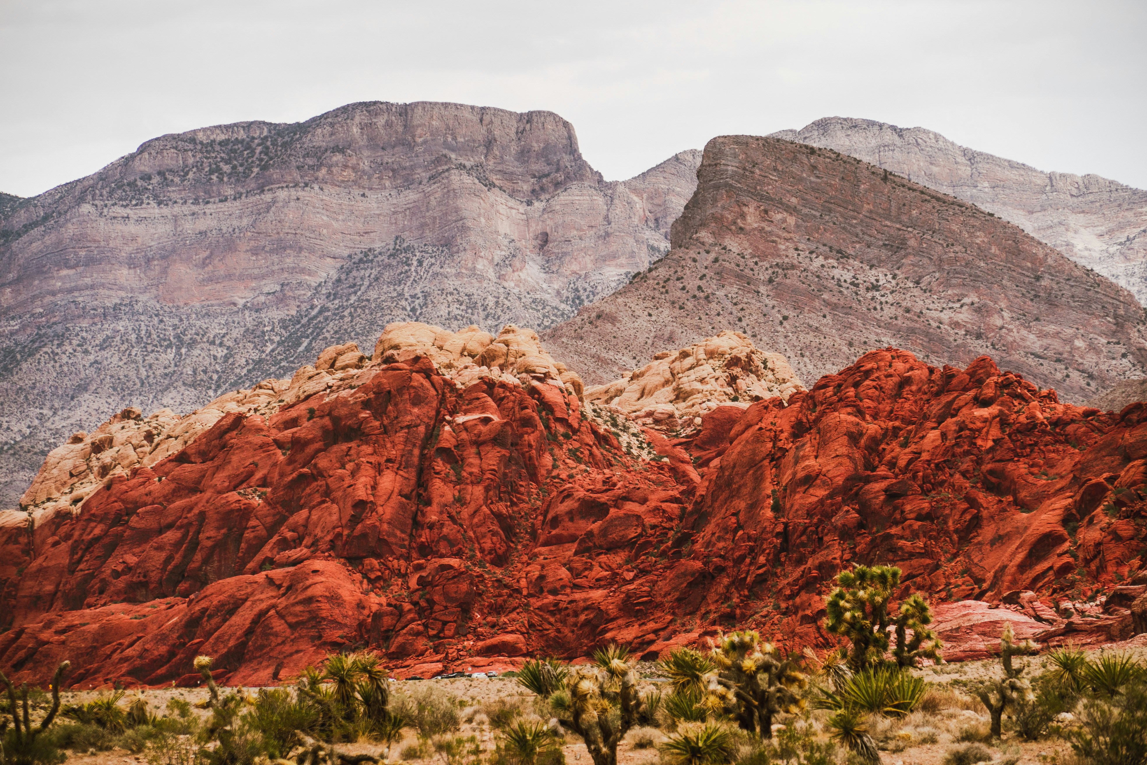 a mountain range with a red rock formation in the foreground, red rock canyon on a cloudy day