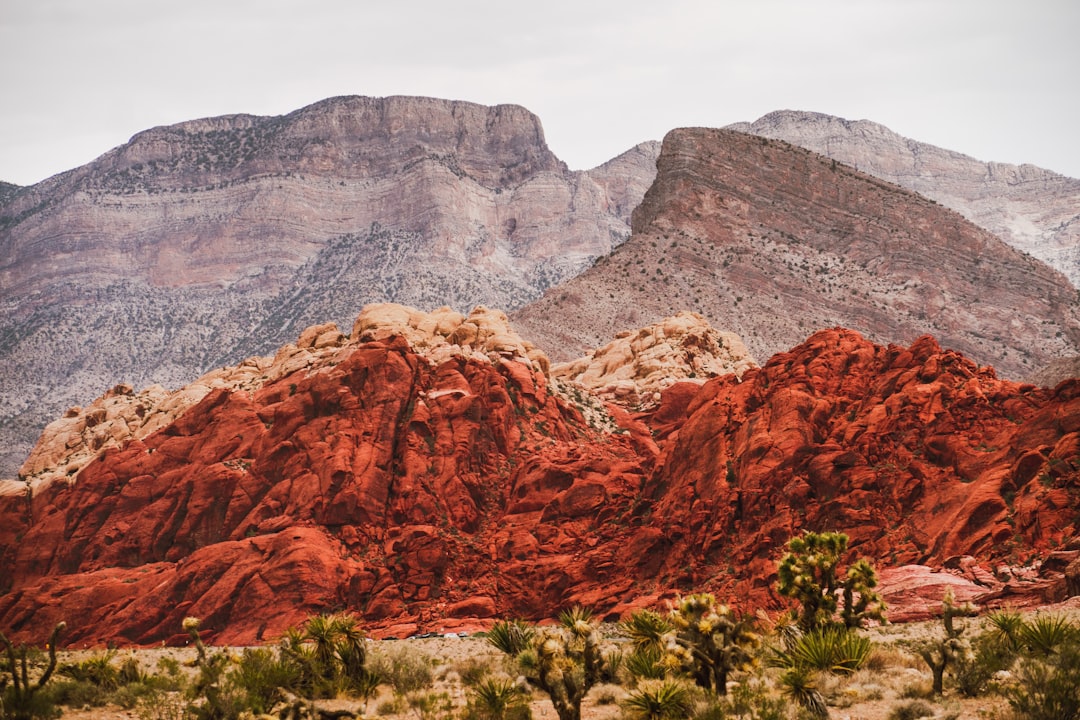 a mountain range with a red rock formation in the foreground, red rock canyon on a cloudy day