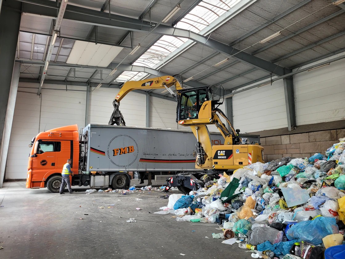 A loader moving a load of compacted waste across the floor of a landfill building.
