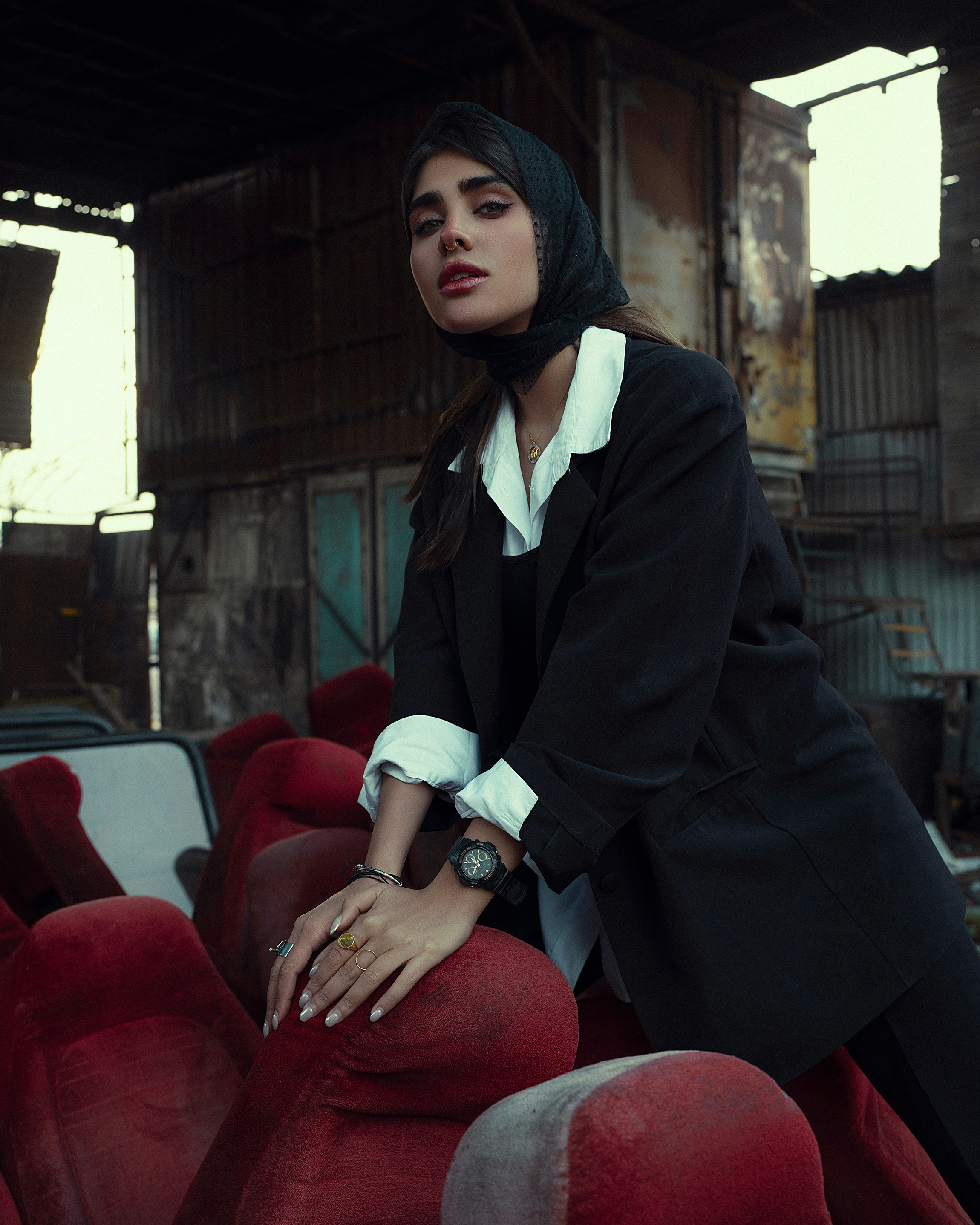 a woman in a black jacket and white shirt leaning on a red chair