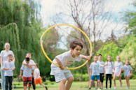 a young boy holding a yellow hula hoop in front of a group of people
