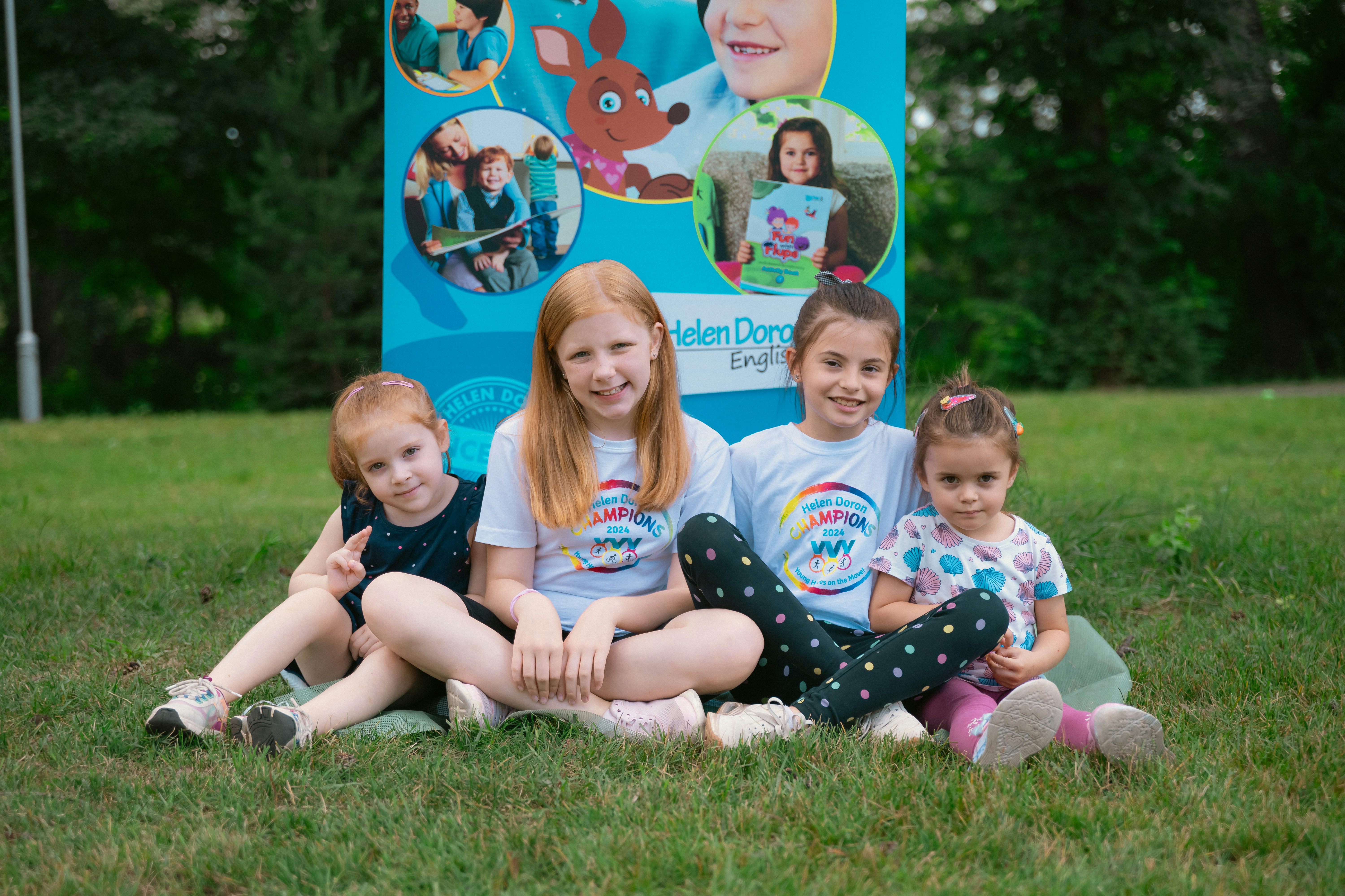 a group of children sitting on the ground in front of a sign