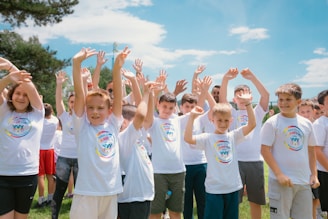a group of children standing in a field with their hands in the air